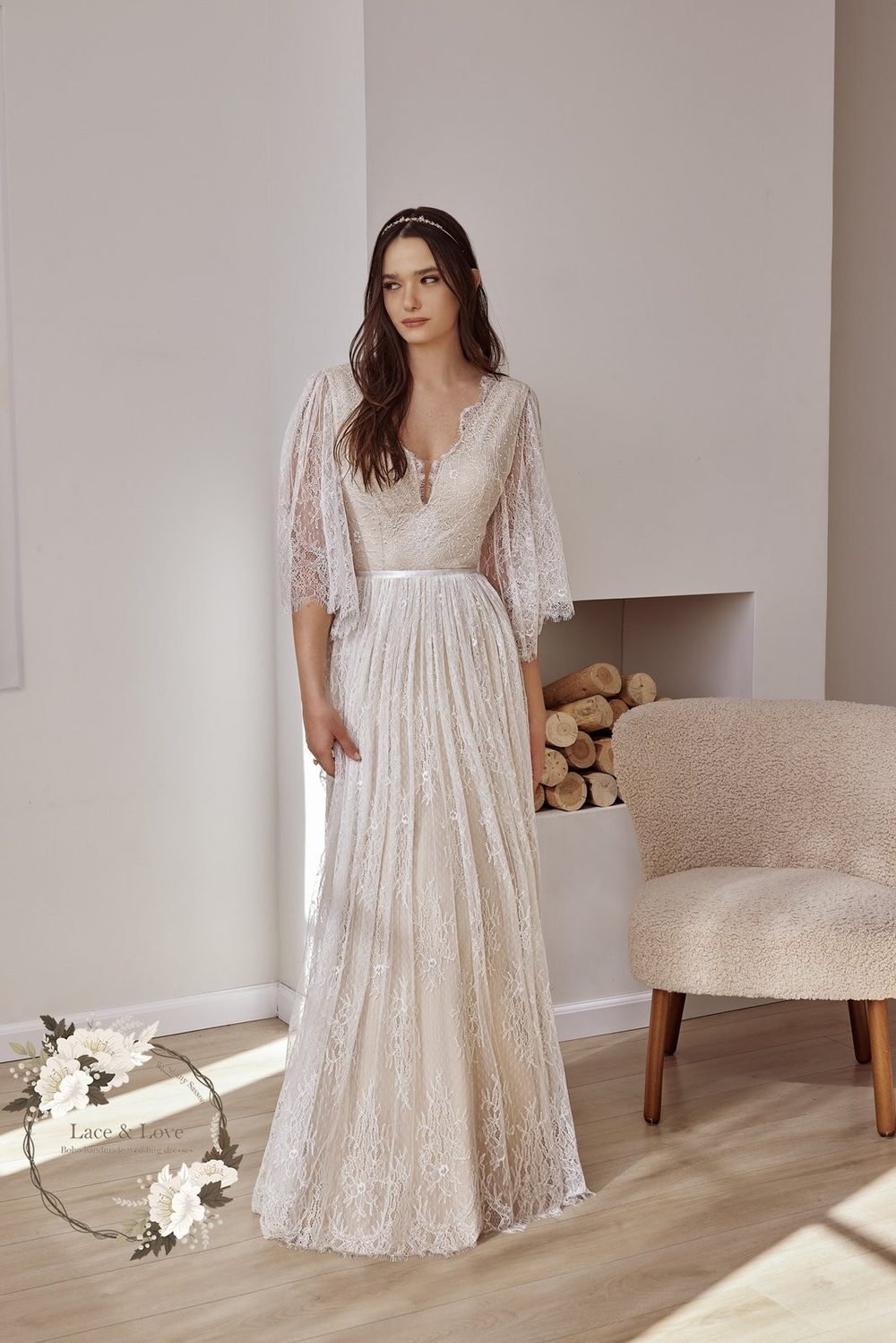 Model in an A-line lace wedding dress with flutter sleeves and a V neckline, standing in a studio.